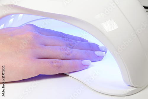 Closeup view of female hands with fresh beautiful pink modern gel polish manicure. Woman puts hand into led uv lamp for curing top cover of nailpolish. Horizontal color photography. photo