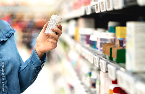 Customer in pharmacy holding medicine bottle. Woman reading the label text about medical information or side effects in drug store. Patient shopping pills for migraine or flu. Vitamin or zinc tablets. photo