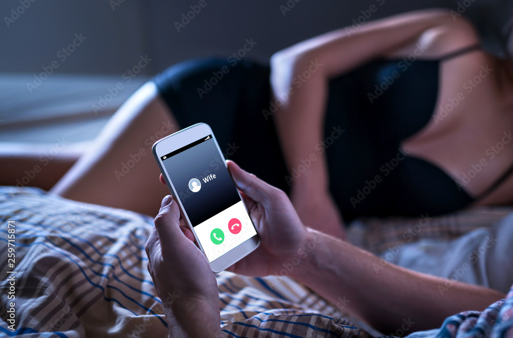 Cheating unfaithful man lying with mistress in hotel bed. Call from wife to mobile phone. Cheater having affair with secret lover and relationship with another woman photo