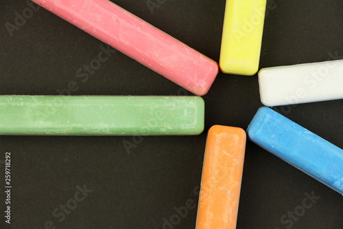 six colored children crayons on black background, blue red green yellow orange white, top view