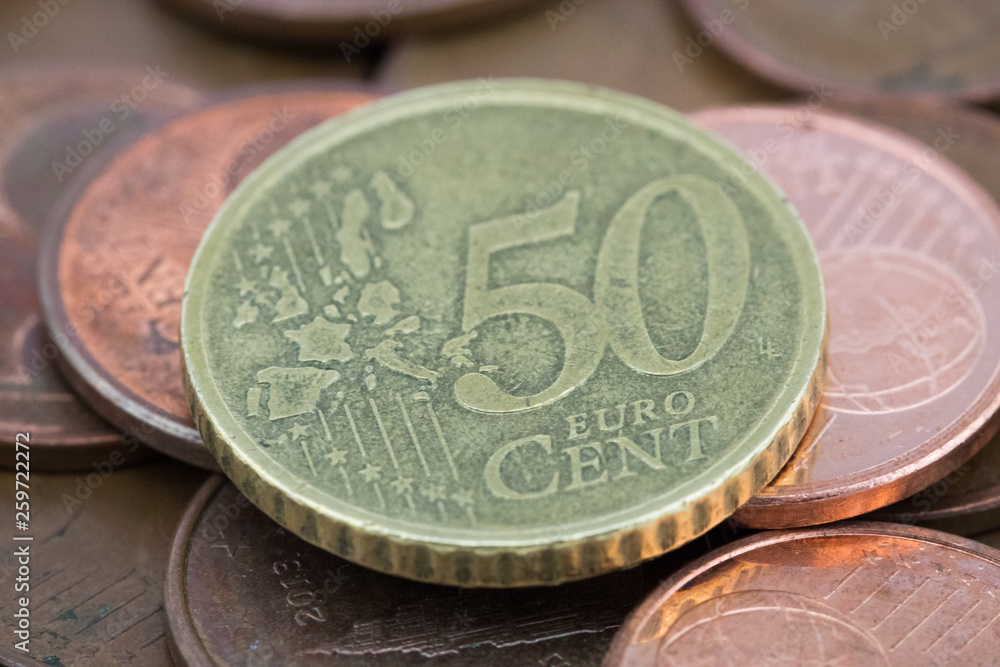 Coin of fifty euro cents on several bronze coins of five euro cents.