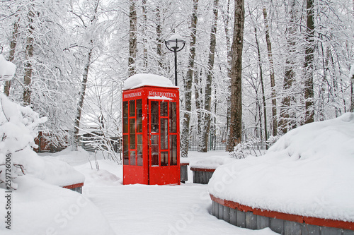Red British telephone booth used as street library in winter (translated from Russian 
