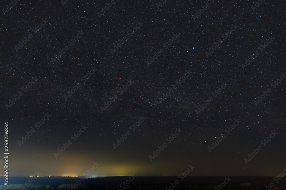 Stars of the Milky Way in the night sky. Light pollution from street lamps above the horizon.