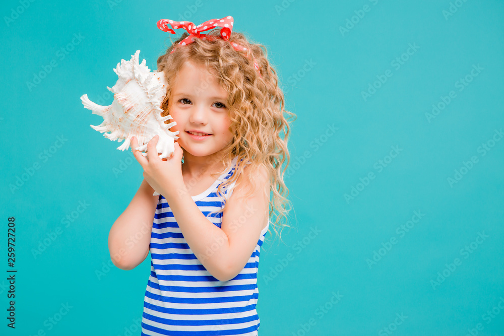 baby girl in striped t-shirt with seashell on blue background. the concept of a holiday by the sea baby girl in striped t-shirt with seashell on blue background. the concept of a holiday by the sea