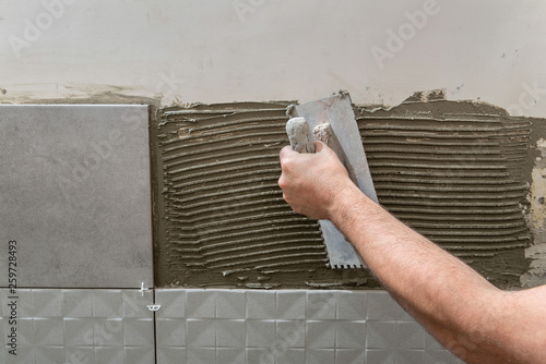 Hand of the tiler laying tile adhesive on the wall with a notched trowel