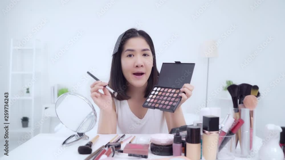 Beauty blogger present beauty cosmetics sitting in front camera for recording video. Happy beautiful young Asian woman use cosmetics review make up tutorial broadcast live video to social network.