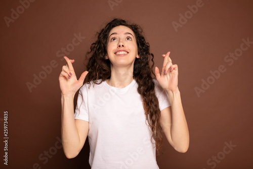Closeup portrait hopeful beautiful woman crossing her fingers, eyes closed, hoping, asking best isolated on brown wall background. Human face expression, emotions, feeling attitude reaction © maryadam