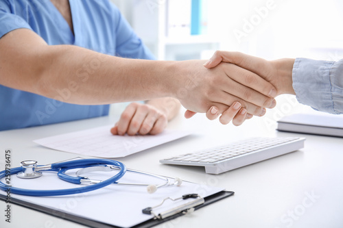 Male doctor shaking hands with woman in clinic
