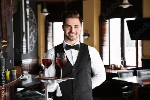 Young male waiter with glasses of wine in restaurant photo