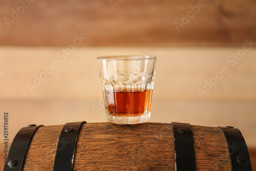 Glass of whisky on barrel against wooden background