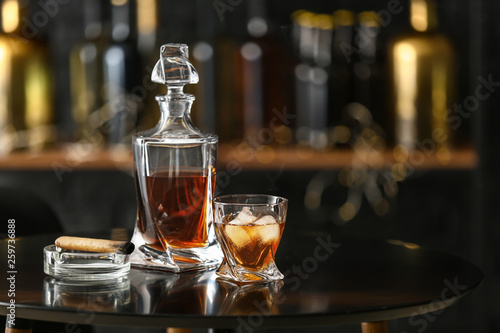 Glass and bottle of cold whiskey with cigar on table in bar