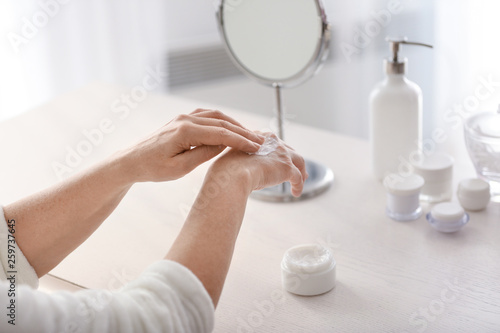 Mature woman applying hand cream at home