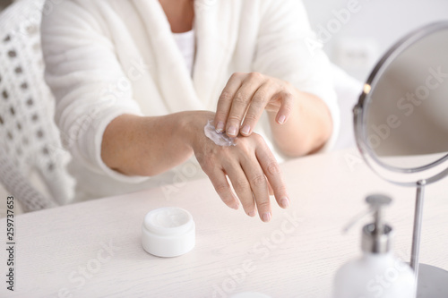 Mature woman applying hand cream at home