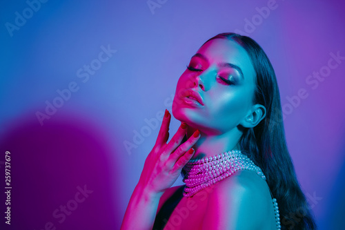 High fashion model in colorful bright neon lights posing at studio. Portrait of beautiful girl with trendy glowing make-up. Art design vivid style.
