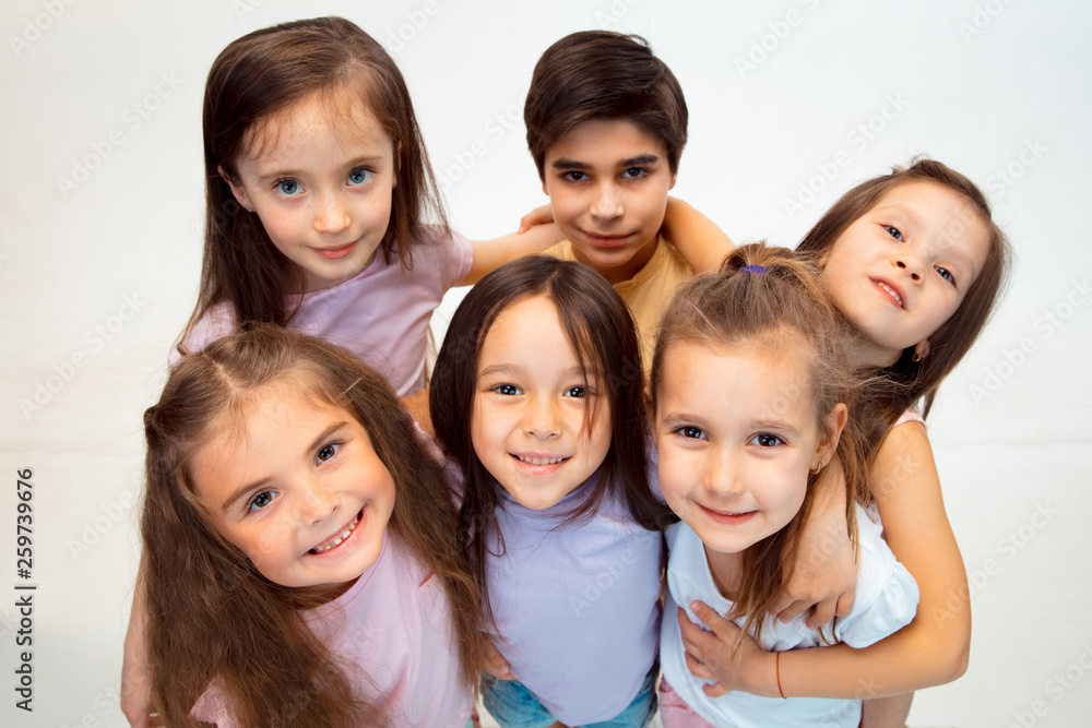 The portrait of happy cute little kids boy and girls in stylish casual clothes looking at camera against white studio wall. Kids fashion and human emotions concept