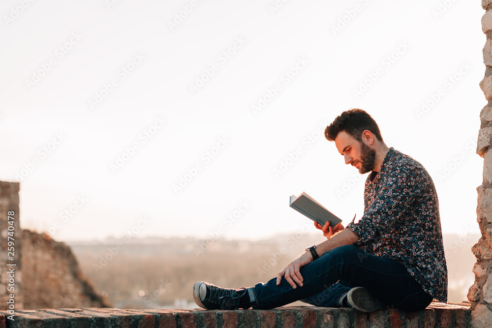 Young man reading a book outdoors in sunset