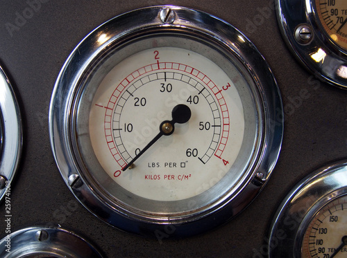 a round metal pressure gauge with a shiny chrome surround on a control panel with other meters