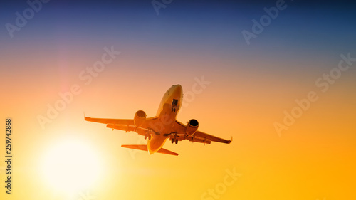 airplane fly against scenic sunset sky background aerial view of passenger plane landing to airport on beautiful sunrise blue and red to orange color sunlight with sun above horizon panorama landscape