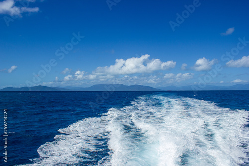 beautiful wake wave behind a big boat for tourist diving at the great barrier reef with blue montains in the background, cairns, australia © Martin