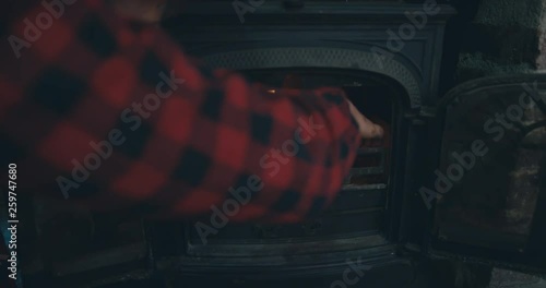 Young man adding kindling to a fire in logburner photo