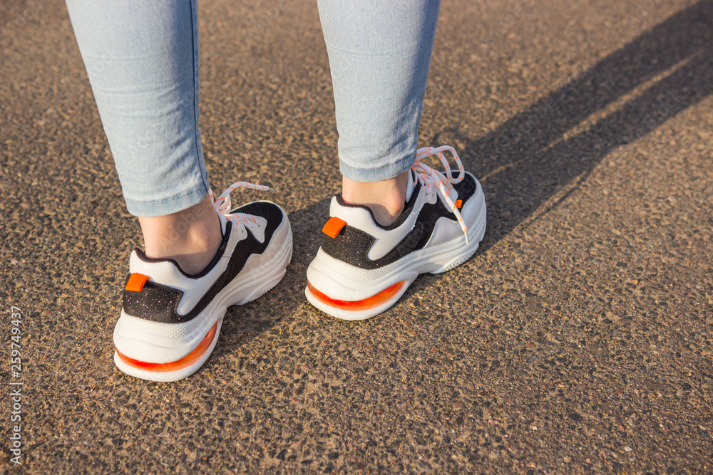 Girl in sneakers and jeans. Several pairs of sports shoes and legs.