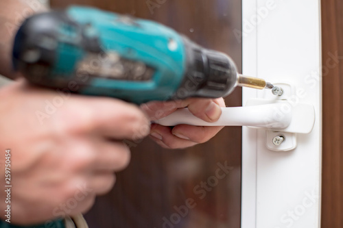 Man holds in his hands an electric screwdriver and is going to screw the handle on the PVC window.