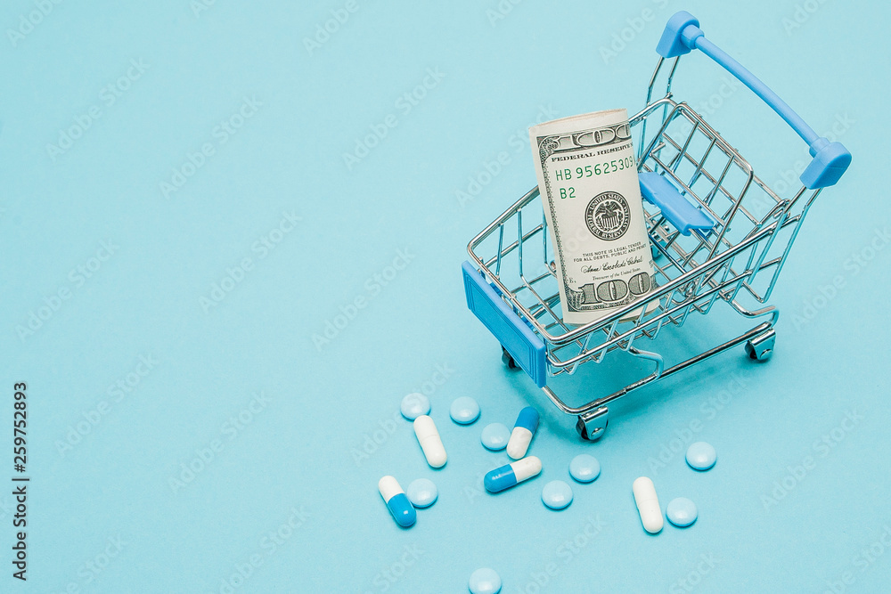 Dollars, pills and shopping cart on a blue background. Pharmacy concept. Copy space
