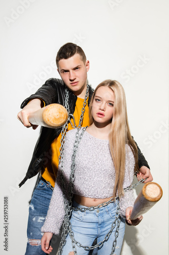 Sport games. Close up fashion portrait of two young cool hipster girl and boy wearing jeans wear. Woman and man with a baseball bats. Studio shot of two cheerful best friends having fun and making
