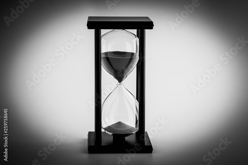 Black and white Hourglass with blue sand running through the glass bulbs ; time passing concept