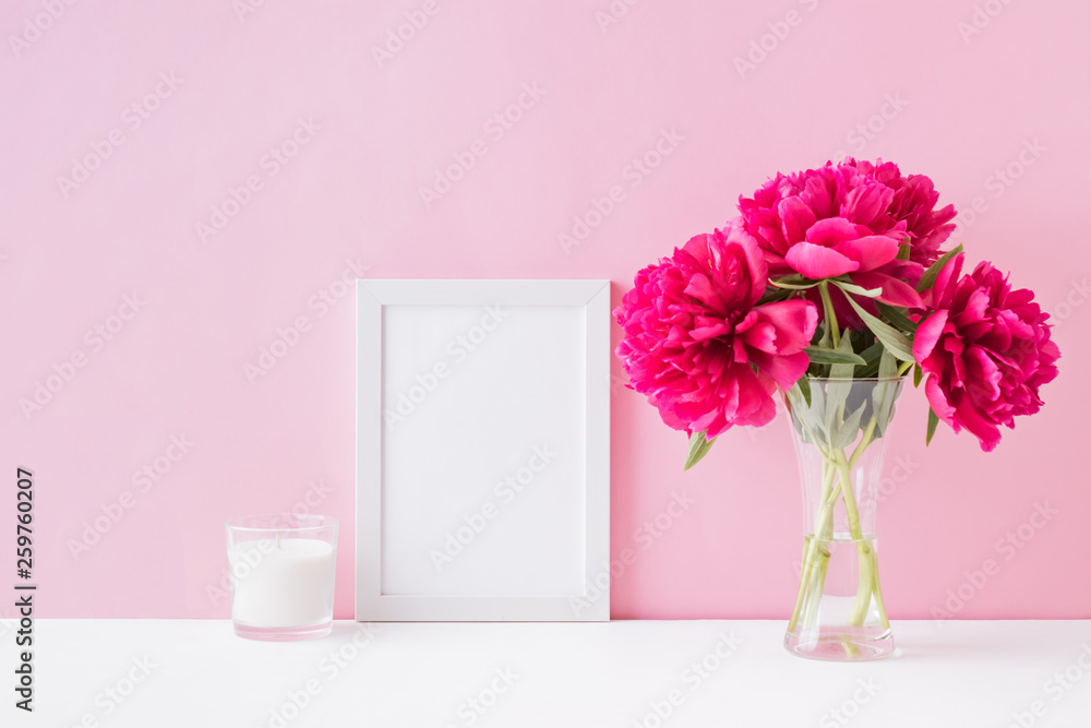 Mockup with a white frame and red peonies in a vase on a pink background Mockup with a white frame and red peonies in a vase on a pink background