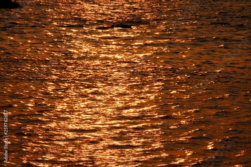 Golden lights reflection with a pattern of colorful water waves splashing on river surface for background texture 