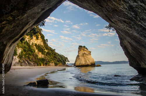 Sunrise at Cathedral Cove with blue sky with white clouds above and reflection in the sea, golden hour