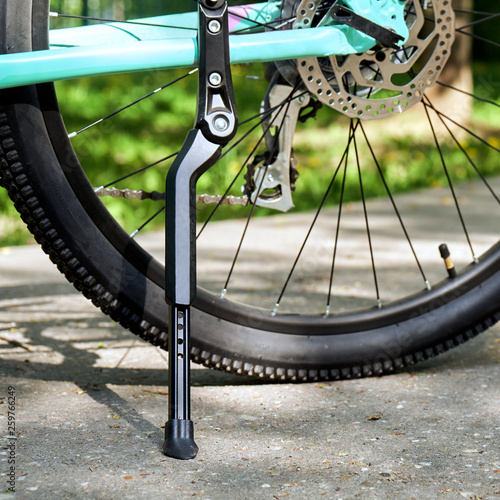 Bicycle kickstand with rear bicycle wheel standing on the asphalt with green grass on the background photo