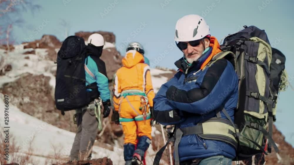 An experienced climber with a gray beard and glasses standing with arms crossed on his chest and enjoying the view An experienced climber with a gray beard and glasses standing with arms crossed on his chest and enjoying the view