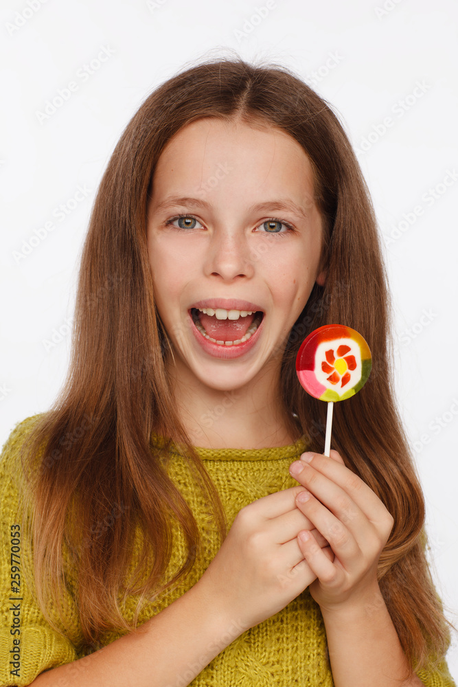 Emotional portrait of an eight-year girl in a yellow-green sweater and with a lollipop in her hands