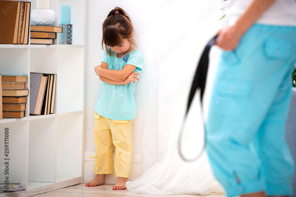 Parental punishment. Child abuse. Mom punish a little daughter with a belt and puts her in a corner. Don't hit the kids, help to protect children Parental punishment. Child abuse. Mom punish a little daughter with a belt and puts her in a corner. Don't hit the kids, help to protect children