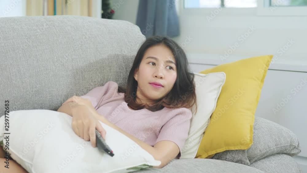 Young Asian teenager woman watching TV at home, female feeling happy lying on sofa in living room. Lifestyle woman relax in morning at home concept. Young Asian teenager woman watching TV at home, female feeling happy lying on sofa in living room. Lifestyle woman relax in morning at home concept.