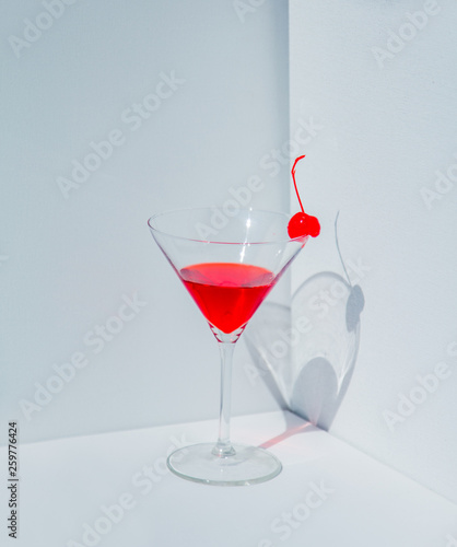 Glass of cocktail and red cherry in a white corner.