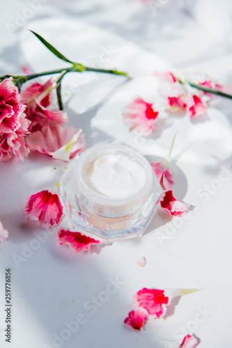 Skin care cream in boolte and dianthus flowers around on white background