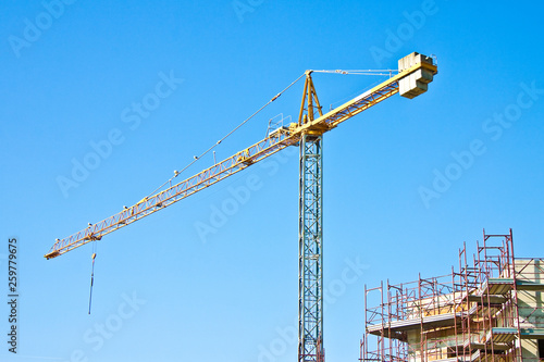 Tower crane in a blue background with metal scaffolding to work on the building facade