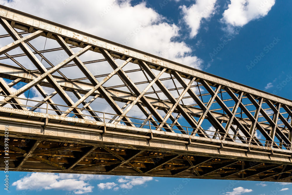 Steel lattice construction of a railway bridge on a background of blue sky with white clouds.