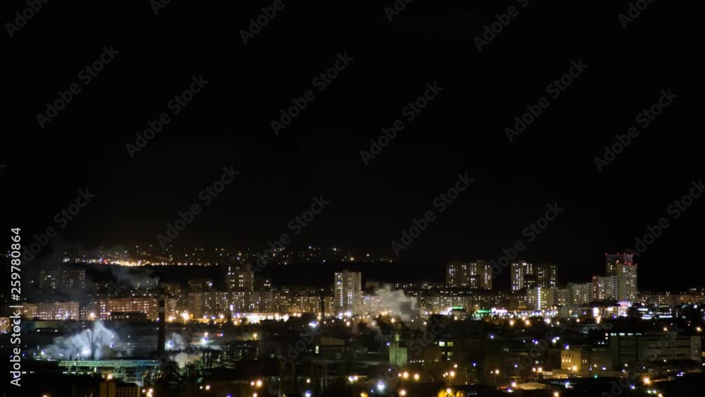 Night city skyline timelapse. Top aerial panoramic view of modern city from tower rooftop. Road junction traffic. Lights flicker in windows. Residential flats,factory pipes with smoke