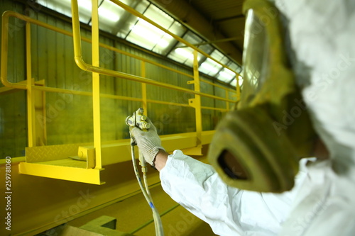 Industrial painting parts. The painter paints the iron element in yellow.