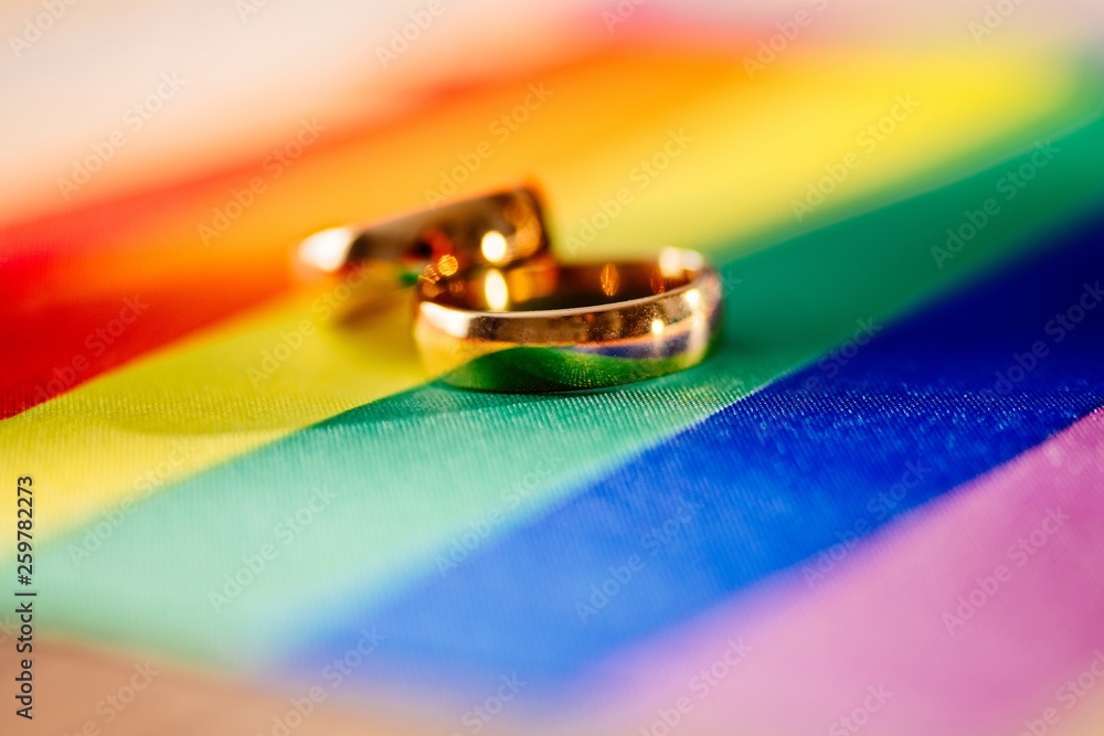 Two gold wedding rings on rainbow lgbt flag. Homosexual marriage.