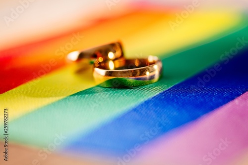 Obraz na płótnie Two gold wedding rings on rainbow lgbt flag. Homosexual marriage. w salonie