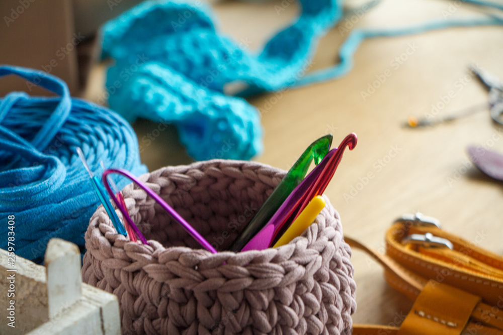 Two-tone knitted basket on a light wooden surface against the background of knitting and details for making handmade knitted bags.