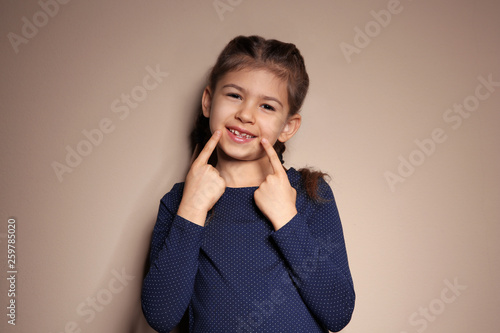 Little girl showing LAUGH gesture in sign language on color background