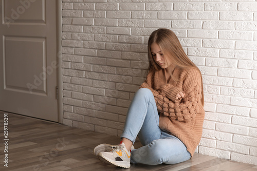 Upset teenage girl sitting alone on floor near wall