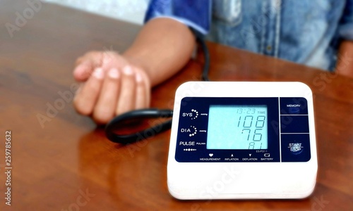 Focus on blood pressure monitor and blurred background of man's arm checking his blood pressure on wooden table, medical and health care concept