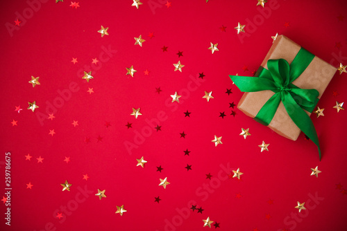 gift box on golden sequins and stars red background. Top view, flat lay. Copyspace for text. Festive holiday background.